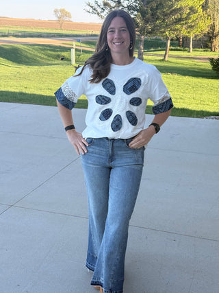 Woman wearing a white shirt with black paw prints and blue jeans standing on a sidewalk.