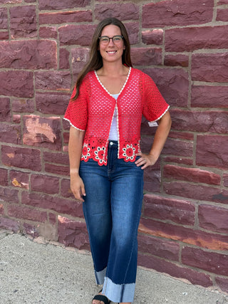 Lady wearing a crochet cardigan with floral hem standing against a brick wall.