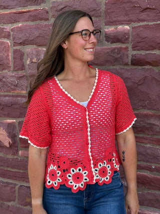 Lady wearing a crochet cardigan with floral hem standing against a brick wall.