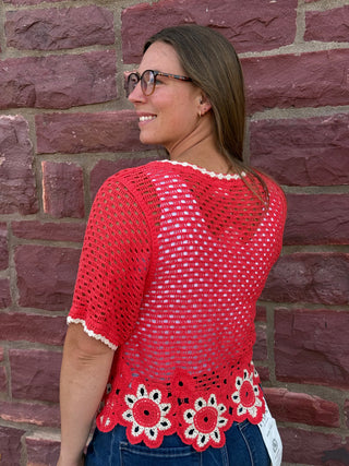 Lady wearing a crochet cardigan with floral hem standing against a brick wall.