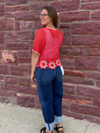Lady wearing a crochet cardigan with floral hem standing against a brick wall.