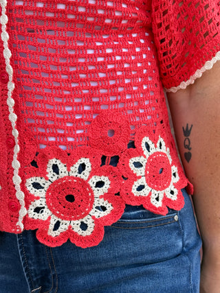 Lady wearing a crochet cardigan with floral hem standing against a brick wall.