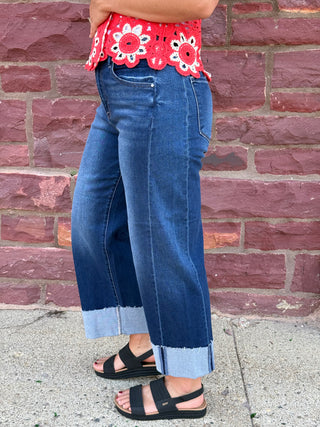 Lady wearing a barrel leg jean with a raw cuffed hem. Standing against a brick wall. 