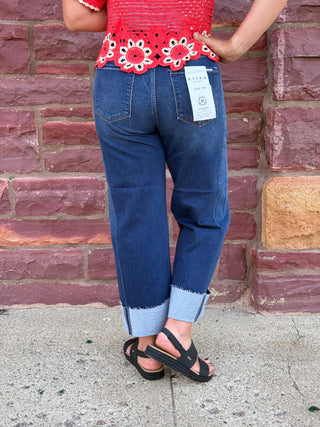 Lady wearing a barrel leg jean with a raw cuffed hem. Standing against a brick wall. 