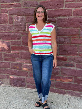 A lady wearing a striped crochet top. She is standing against a brick wall.