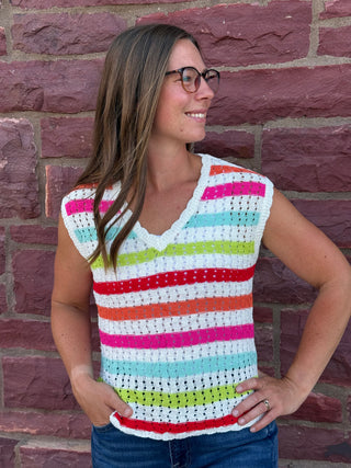 A lady wearing a striped crochet top. She is standing against a brick wall.