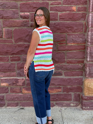 A lady wearing a striped crochet top. She is standing against a brick wall.