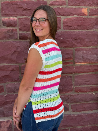 A lady wearing a striped crochet top. She is standing against a brick wall.