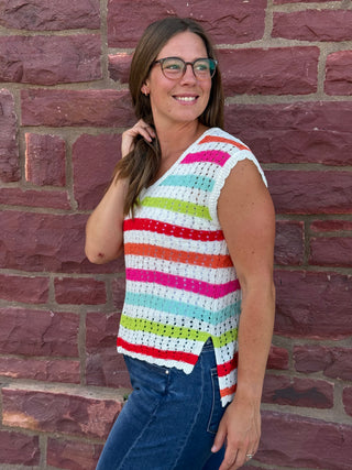 A lady wearing a striped crochet top. She is standing against a brick wall.