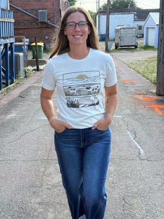 A lady wearing a graphic tee with outdoor scenes. Standing outside.