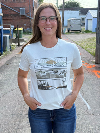 A lady wearing a graphic tee with outdoor scenes. Standing outside.