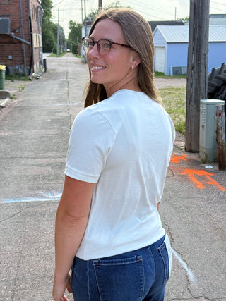 A lady wearing a graphic tee with outdoor scenes. Standing outside.