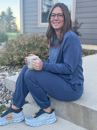 Person wearing a blue outfit sitting on steps holding a mug.
