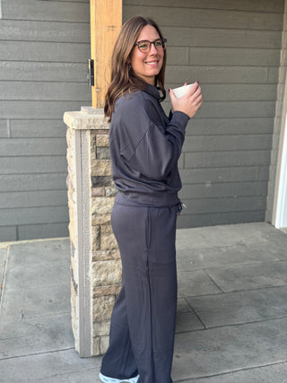 Woman in dark gray tracksuit holding a white cup outdoors.