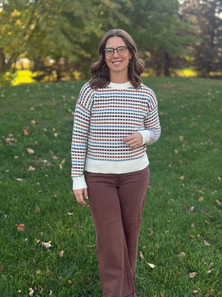 Front view of a model wearing a multicolor striped cream sweater with brown pants.