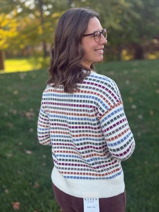 Close-up back view of a cream sweater with blue, burgundy, green, and rust rectangular stripes.