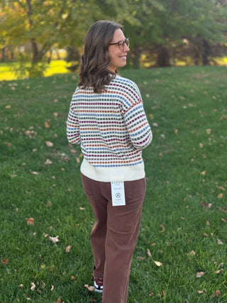 Back view of a model wearing a cream sweater with multicolor rectangular stripes and ribbed trim.