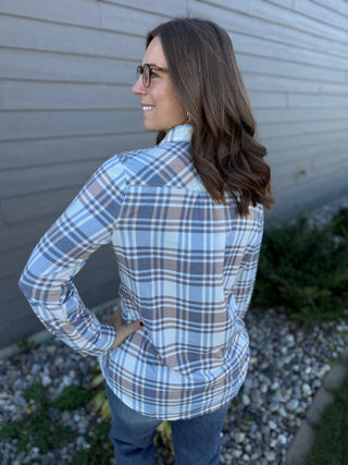 Woman wearing a blue plaid shirt standing against a gray wall.