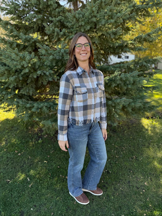 Woman wearing a plaid shirt and jeans standing in a grassy area with trees.