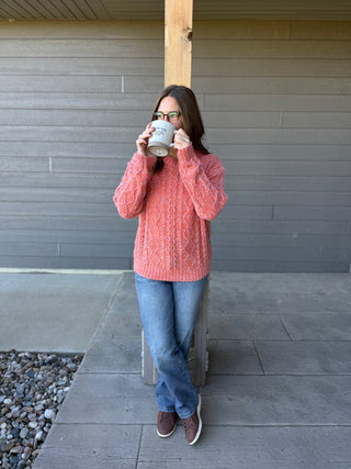 Woman in a pink sweater and jeans drinking from a white mug outdoors.