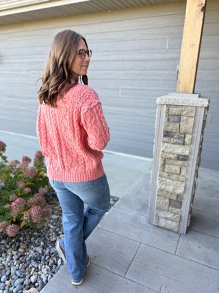 Woman wearing a pink sweater and blue jeans standing outside a house.