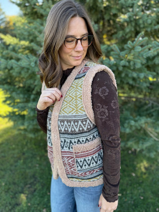 Woman wearing a patterned vest outdoors with trees in the background