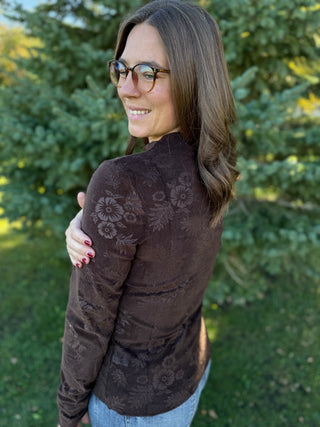 Woman wearing a brown floral-patterned sweater standing outdoors with greenery in the background