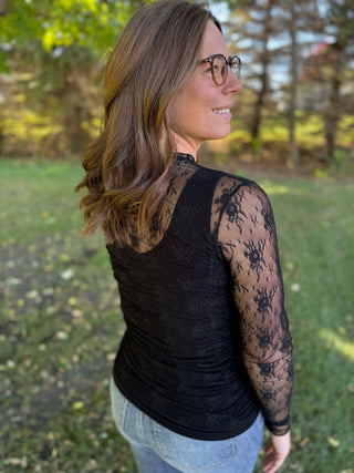 Woman wearing a black lace sleeve top outdoors with trees in the background
