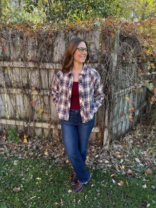 Woman standing outdoors in front of a wooden fence with foliage