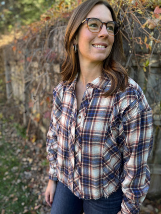 Woman wearing a plaid shirt standing outdoors with trees in the background