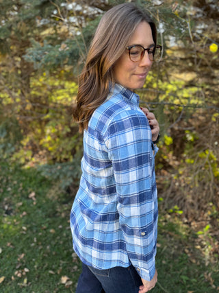 Woman wearing a blue plaid shirt standing outdoors with trees in the background