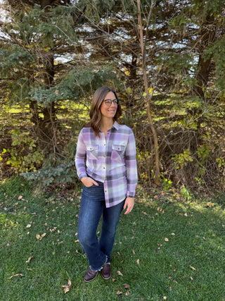 Woman wearing a plaid shirt and jeans standing in a grassy area with trees in the background