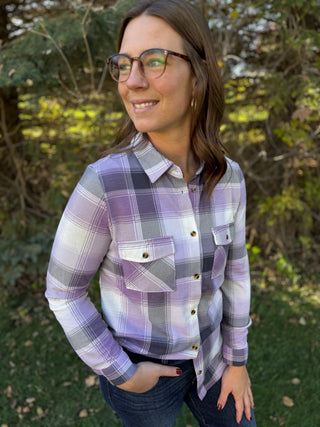 Woman wearing a plaid shirt outdoors with greenery in the background
