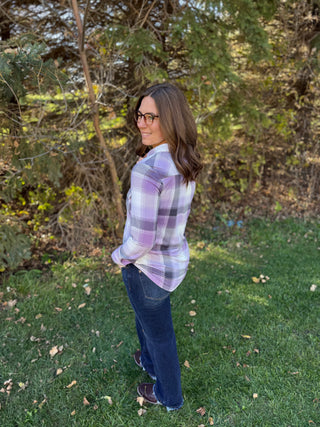 Woman wearing a plaid shirt and jeans standing in a grassy area with trees in the background