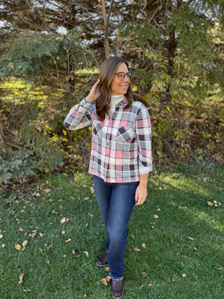 Woman wearing a plaid shirt and jeans standing in a grassy area with trees in the background