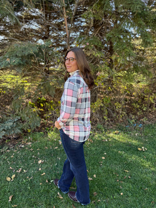 Woman wearing a plaid shirt and jeans standing in a grassy area with trees in the background
