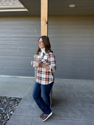 Woman in plaid shirt and jeans holding a mug, standing on a patio.