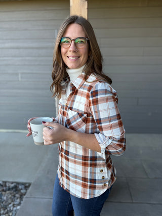 Woman in plaid shirt holding a coffee cup against a neutral wall.