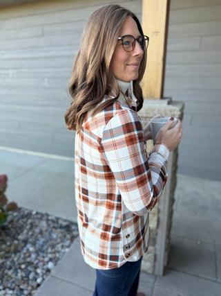Woman wearing a plaid shirt and holding a mug outdoors.