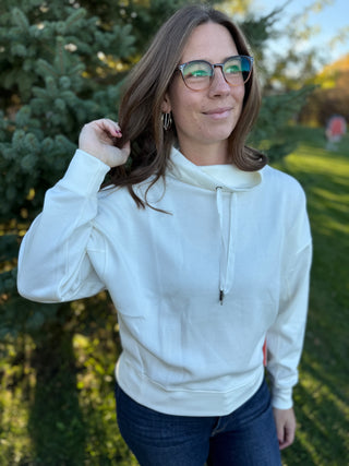 Woman wearing a white hoodie and glasses outdoors with trees in the background