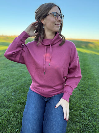 Woman wearing a pink hoodie and blue jeans standing in a grassy field.