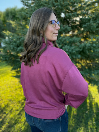 Woman wearing a pink jacket standing in a field with trees in the background