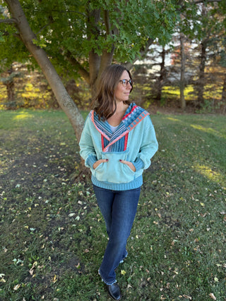 Woman wearing a light blue sweater with colorful patterns in an outdoor setting
