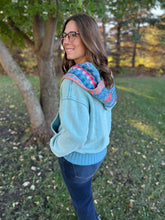Load image into Gallery viewer, Woman wearing a light blue hoodie with a colorful pattern on the hood, standing outdoors in a park.
