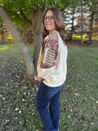 Woman wearing a patterned shirt and jeans standing outdoors near a tree