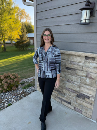 Woman standing outside a house wearing a patterned shirt and black pants.