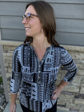 Woman wearing a patterned shirt standing against a brick wall.