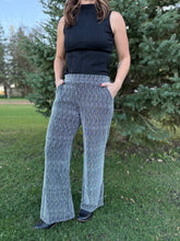 Load image into Gallery viewer, Person wearing a black sleeveless top and gray patterned pants standing outdoors with trees in the background.

