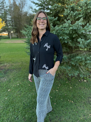 Woman wearing a black shirt with white designs and gray pants standing outdoors.