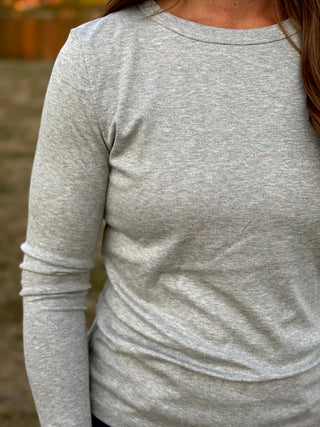 A close-up of a person wearing a light heather gray long-sleeve crewneck shirt, showing the fabric texture and fit.